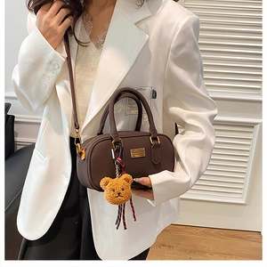 Detail of dark brown leather handbag with gold logo and plush bear charm on white suit