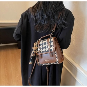 Detail of a brown quilted crossbody backpack with a knitted rabbit charm and logo