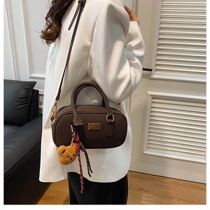 Detail of dark brown leather Boston bag with plush bear charm and crossbody strap