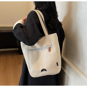 Detail of beige canvas tote bag with blue wavy stitching and embroidered puppy graphic