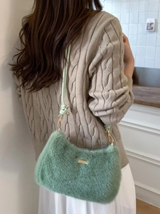 Sac bandoulière en peluche vert avec logo doré sur fond de pull en maille torsadée