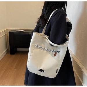 Detailed close-up of white canvas tote bag featuring blue zigzag stitching and dog embroidery