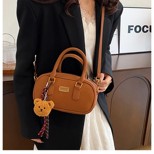 Detail of brown leather handbag with gold logo plate and cute plush bear charm