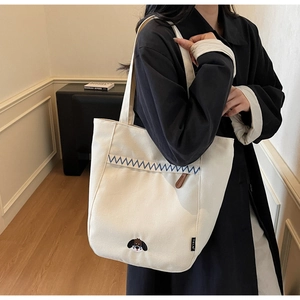 Detail of white canvas tote bag featuring blue zigzag stitching and dog head embroidery