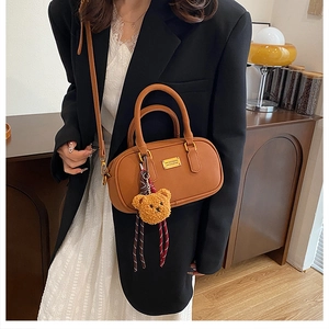 Detail of caramel leather bowling bag with gold logo and brown plush bear charm