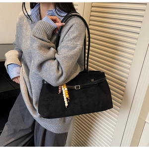 Detail of black suede tote bag featuring a leather strap with colorful beaded pendant charm