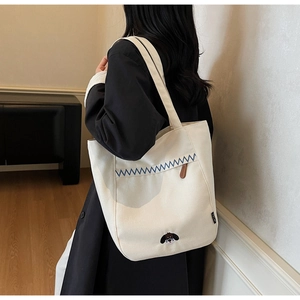 Detailed close-up of a cream canvas tote bag featuring dog embroidery and blue wavy stitching