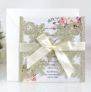 Close-up of laser-cut snowflake invitation with gold glitter and white satin bow