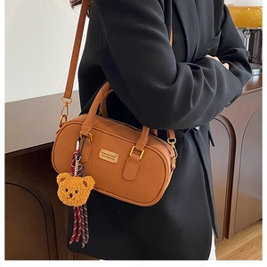 Detail of a brown leather Boston handbag with a plush bear charm and golden hardware