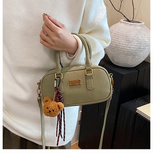 Detailed close-up of sage green bowling bag featuring a plush bear charm and metallic logo
