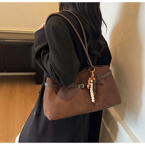 Detail of dark brown suede shoulder bag with thin leather straps and ethnic bead charm
