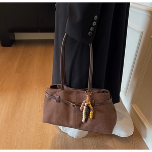 Close-up of brown suede tote bag with leather straps and decorative beaded charm detail