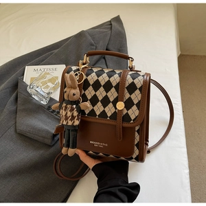 Detail of retro plaid stitching leather handbag with a plush bunny charm and gold clasp