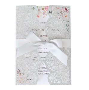 Detail of laser-cut glitter wedding invitation with silver envelope and white satin bow