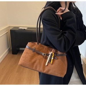 Detail of caramel suede tote bag with beaded pendant worn by a model in a black coat