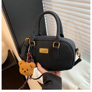 Close-up of black Boston bag with golden hardware and a cute brown plush bear charm