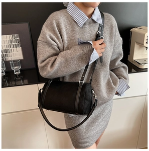 Detail of a black matte cylinder crossbody bag with leather straps on a stylish model