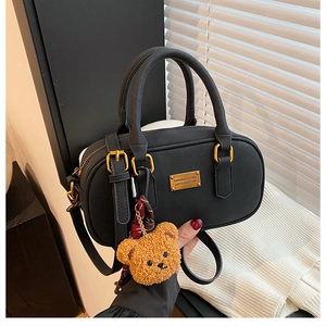 Detail of black bowling bag with golden logo plate and cute brown plush bear charm