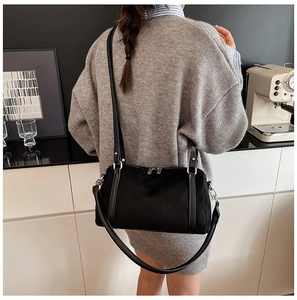Minimalist black matte crossbody bag with silver zippers shown in a lifestyle cafe setting