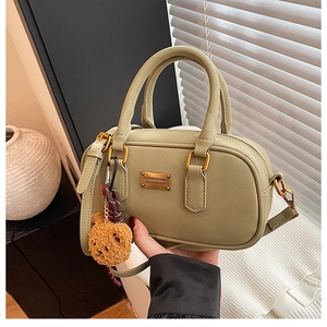 Detail of pea green Boston bag with golden metal plate and cute brown bear pendant charm