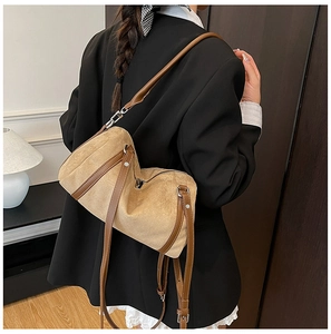 Brown suede crossbody pillow bag shown on shoulder in a minimalist indoor setting