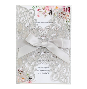 Detail of silver glitter laser cut wedding invitation with grey ribbon and floral card