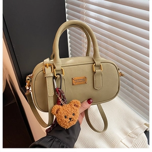 Detailed view of olive green bowling bag with gold plaque and brown plush bear charm