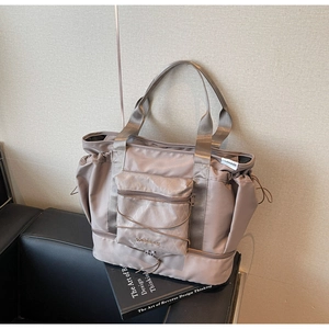 Detail of taupe travel tote showing geometric embossed front pocket and elastic cords