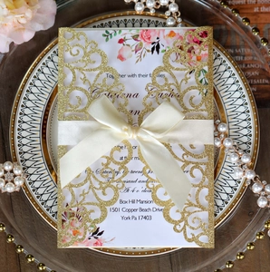 Macro detail of laser-cut glitter gold wedding invitation with a white satin ribbon