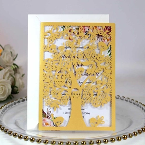 Close-up of golden laser-cut tree of life invitation card with white insert and envelope