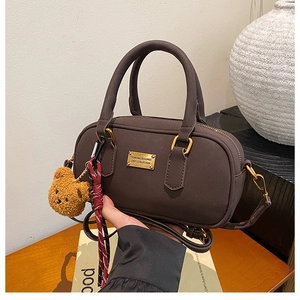 Close-up of brown crossbody bowling bag with golden metal plaque and plush bear charm