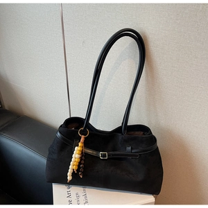 Detailed close-up of a black suede hobo bag featuring a gold buckle and beaded charm accessory
