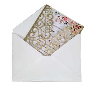 Close-up of laser-cut gold glitter wedding invitation with floral insert and white envelope