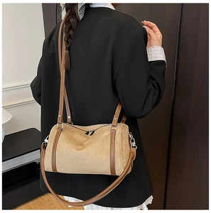 Detail of beige suede cylinder shoulder bag with leather straps on model in black blazer