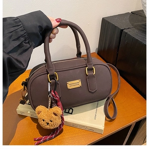 Detail of dark brown faux leather bowling bag with gold logo and plush bear charm