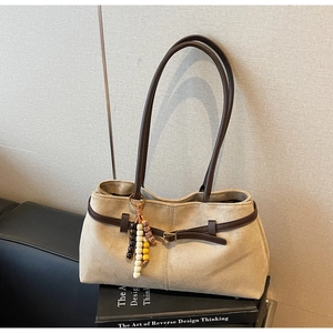 Detail of beige suede tote bag with brown leather straps and wooden bead accessory