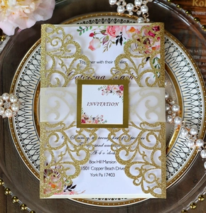 Detail of laser-cut gold glitter wedding invitation with floral inner card on a plate