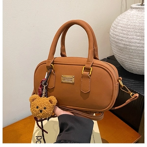 Close-up of brown PU leather Boston bag featuring metal logo and cute teddy bear charm