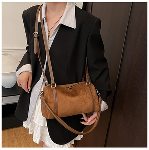 Detail view of a warm brown suede cylinder bag with adjustable dual straps and silver zippers