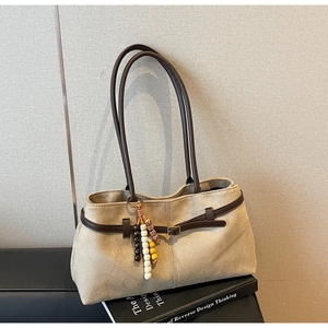 Detail of beige suede shoulder bag featuring brown leather straps and wooden bead charm