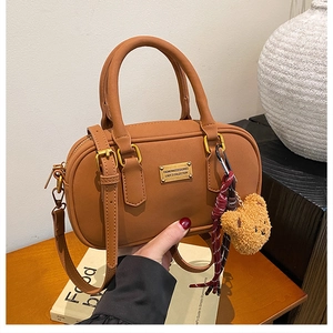 Detailed view of brown bowling bag with gold logo plate and cute teddy bear keychain