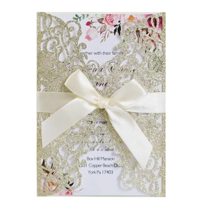 Detailed laser-cut gold glitter wedding invitation with satin bow and floral inner card