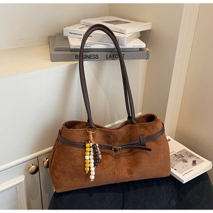 Detailed shot of brown suede tote bag featuring leather buckle and wooden bead tassel