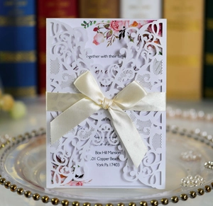 Close-up of laser cut wedding invitation with beige satin bow and floral inner page detail