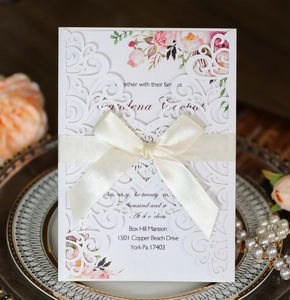 Detail of laser-cut wedding invitation with cream ribbon on decorative gold-rimmed plate