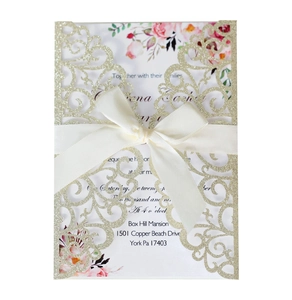 Detail of laser-cut glitter wedding invitation with floral insert and satin ribbon bow