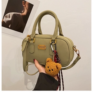 Close-up of sage green bowling handbag with gold metal logo and plush bear charm