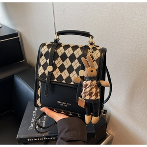 Detail of checkered square backpack with brand logo and cute rabbit charm on leather sofa
