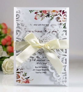 Laser cut wedding invitation with white floral design and elegant silk ribbon bow