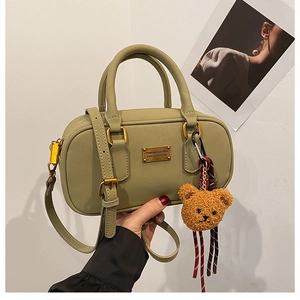 Detail view of olive green bowling bag with fuzzy bear charm and gold metal branding plate